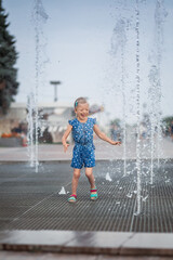 Little girl having fun in fountains. Hot summer weather in city. Little girl running near fountains in hot weather. Child running between water jets of fountains