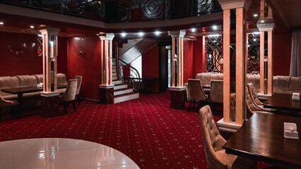 luxury premium restaurant. restaurant interior in red and yellow colors. columns in the restaurant. upholstered furniture, armchairs, sofas, wooden tables, red carpets. cozy environment.