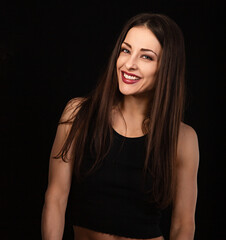 Fototapeta premium Beautiful happy young woman with toothy smile in black top on black background with empty copy space. Closeup portrait of natural happiness.