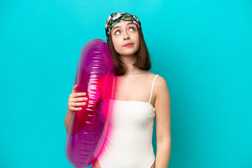 Young Ukrainian woman holding air mattress isolated on blue background and looking up