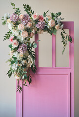 Fototapeta na wymiar Pink wooden doors in vintage style, surrounded on one side by pink roses, peonies, various flowers. With space to copy. High quality photo