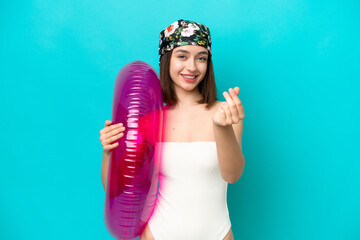 Young Ukrainian woman holding air mattress isolated on blue background making money gesture