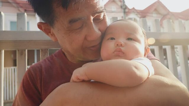 Happy Warm Asian Old Man and Baby Kid in Domestic Comfort. Wrinkled Skin of Grandfather or Black dyed Haired Aged Parent in Casual Summer Day Light. Gentle Embrace and Smile of 60s Retired Grandparent