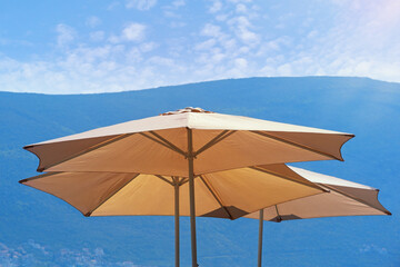 Fototapeta na wymiar Sun umbrellas against mountains on sunny day. Montenegro. Vacations concepts