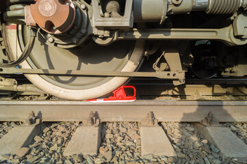 Red railway brake shoe under the iron wheel of electric freight locomotive on rail. Parking brake device. Selective focus