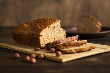 Homemade banana bread with hazelnuts on a cutting board on a rustic wooden background. Vegan pastries. Healthy breakfast. Selective focus.


