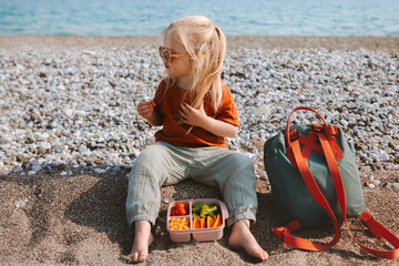 Kid with lunch box outdoor eating vegan food on beach healthy lifestyle summer vacations child girl...