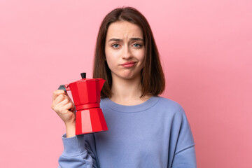 Young Ukrainian woman holding coffee pot isolated on pink background with sad expression