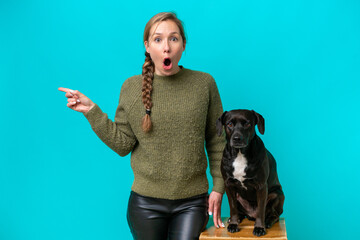 Obraz premium Young caucasian woman with her dog isolated on blue background surprised and pointing side