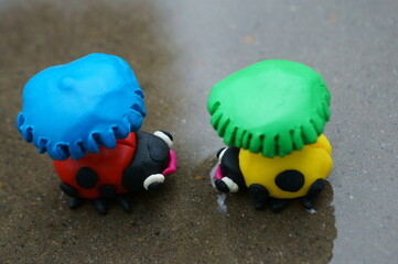 Obraz premium Figures of two ladybirds with umbrellas stand in a puddle.