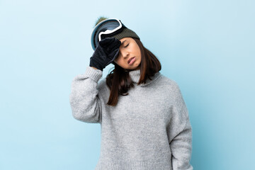 Mixed race skier girl with snowboarding glasses over isolated blue background with tired and sick expression.