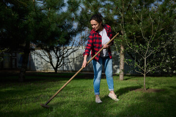 Calm joyful female housewife gardener cleans the garden of her country house with a rake, collects...
