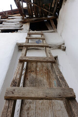 classic handmade wooden ladder for climbing on the roof,The old village house and the wooden ladder placed on its roof,