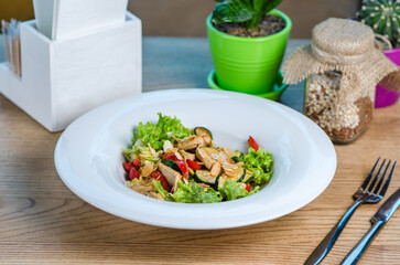 Warm salad with turkey, lettuce, bell pepper, zucchini and almond flakes. Snack in a cafe or restaurant in a white plate on a wooden table.