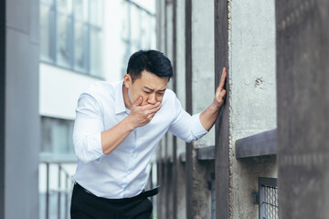 Fototapeta na wymiar Sick businessman, Asian man has severe nausea outside near the office