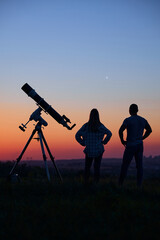 Couple stargazing together with a astronomical telescope.