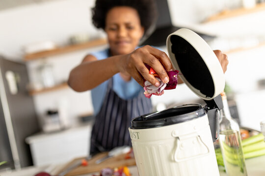 African american mid adult woman putting waste in dustbin while cooking food at home