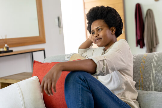 Thoughtful mid adult african american woman sitting on sofa at home