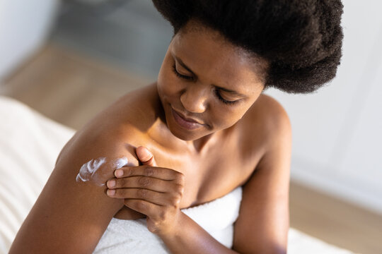 African american mid adult woman applying moisturizer on arm at home