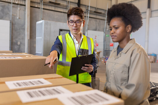 Asian male manager pointing towards cardboard box while guiding african american young female worker