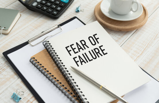 FEAR OF FAILURE text on notepad lying on office table together with calculator, cactus, pencils and paper clips