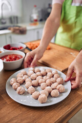 Adult woman, cooking a Spanish dish, meatball stew. Making the meatballs to put in the pot. Wearing an apron, wearing glasses and cooking utensils.