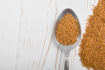 grains for brewing buckwheat tea in a spoon and scattered on a white wooden background