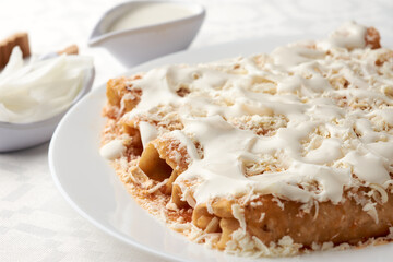 Enchiladas with cheese and cream, Veracruz style. a hand is shown pouring cream onto the enchiladas. mexican grastononomy