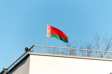 Flag of Belarus. This is the official state symbol of Belarus. Approved June 7, 1995. The Belarusian red-green flag fluttering in the wind on a building against a blue sky.