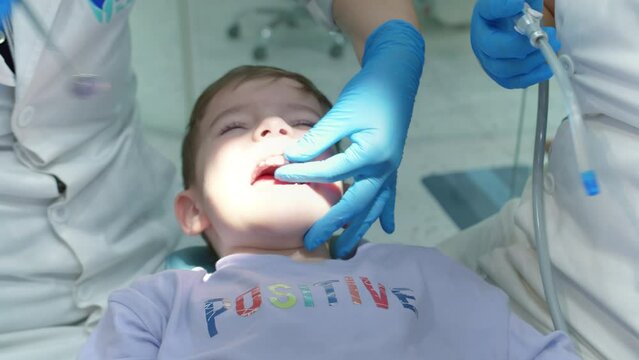 Woman dentist examines baby teeth of child little boy patient in clinic. Female professional dentist at work. Dental examination concept. Work Dentist with Children. Healthcare and Medicine Concept.