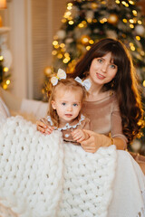 cute mother and daughter on a chair in a room with Christmas garlands. 
