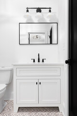 A modern, white bathroom with a patterned tile floor, white vanity cabinet, and black light fixture, door, and faucet.