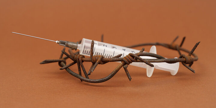 On the brown surface is a drug syringe with barbed wire around it.