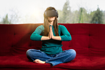 Woman in VR glasses sits in a lotus yoga position joining hands - virtual meditation - Girl taking yoga classes in virtual reality - lifestyle and technology concept