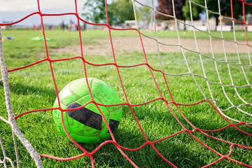 Close-up of soccer ball in the gate after goal, equipment on green grass prepared for training in...