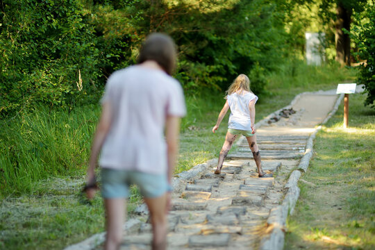 Two sisters on tactile path in barefoot park created to feel the ground and other materials with bare feet. Strengthen foot and leg muscles by walking on uneven surface.