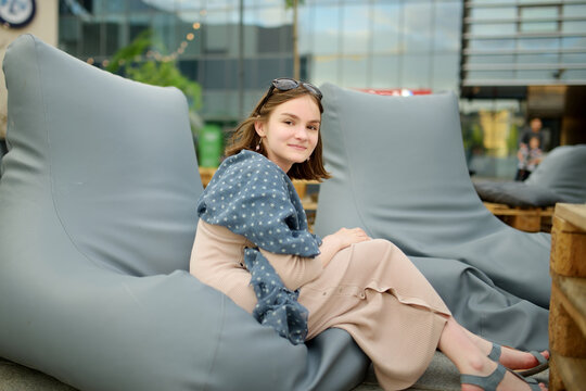 Cute teenage girl relaxing on a sitting pillow in outdoor cafe in Vilnius, Lithuania on warm and sunny summer day.