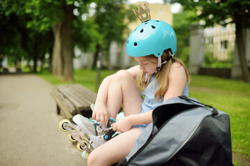 Young girl putting on her inline roller skates on beautiful summer day in a park. Child enjoying...