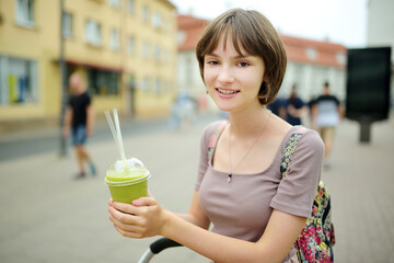 Pretty teenage girl drinking tasty fresh smoothie outdoors on warm sunny summer day. Child eating sweets.