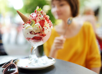 Pretty teenage girl eating tasty fresh ice cream outdoors on sunny summer day. Delicious and appetizing ice cream dessert on a table.