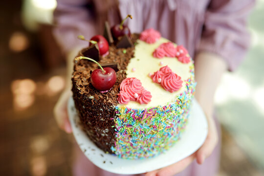 Delicious two-sided homemade birthday cake. Beautiful chocolate and cherry cake covered with choco sprinklers. Tasty light pink cake with colourful sprinkles.