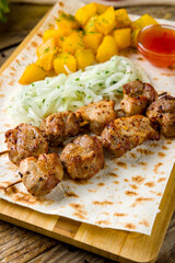 Kebab of pork with potatoes, onion and sauce on the board macro close up vertical