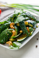broken cucumbers with peanuts and cashew on white marble table selective focus vertical