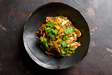 chicken wok noodles with vegetables on black bowl on dark stone table top view