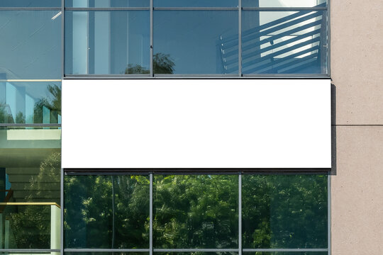 Blank white advertising banner on the wall of modern building with glass facade