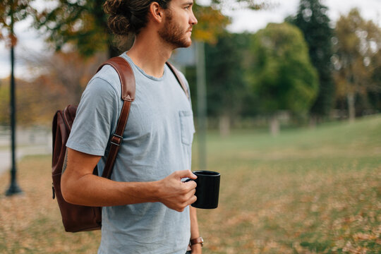 man wearing backpack standing outside with a cup of coffee