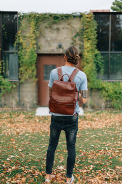 man wearing man bun and backpack looking at old building with vi