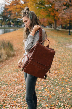 woman with top knot putting on backpack outside on a fall day in