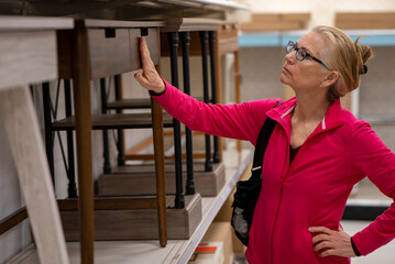 Closeup of pretty, blonde, mature woman inspecting the desks and quality of furniture in a store display.
