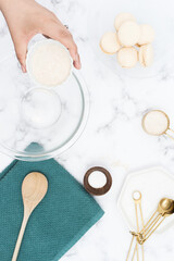 female hand adds flour to mixing bowl surrounded by baking utensils